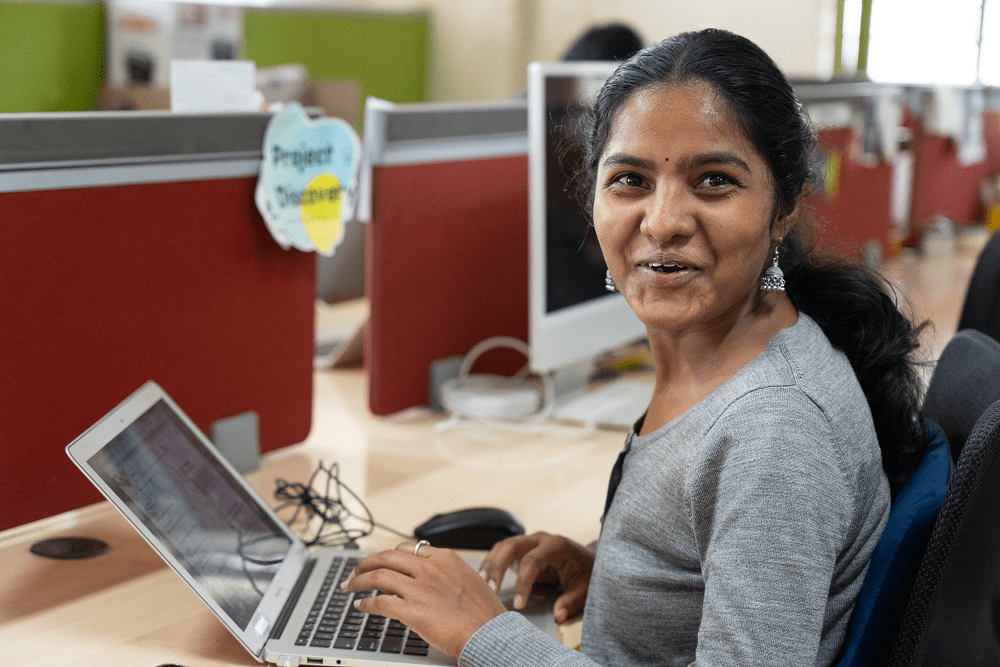 A woman with a disability smiling while working at a computer in an office environment.