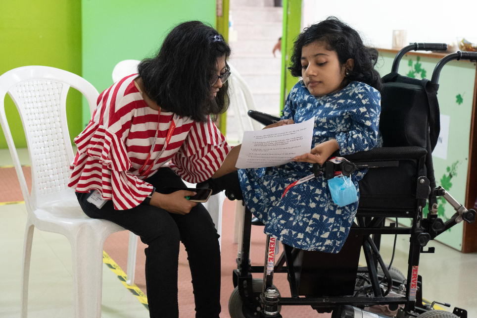 Two women in conversation, one using a wheelchair, reviewing a document together