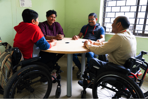 Group of wheelchair users and a trainer seated in a roundtable discussion